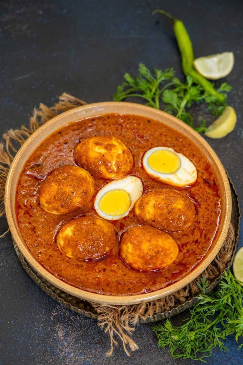 A bowl of Indian egg curry with whole and halved boiled eggs in a rich, reddish-brown gravy.