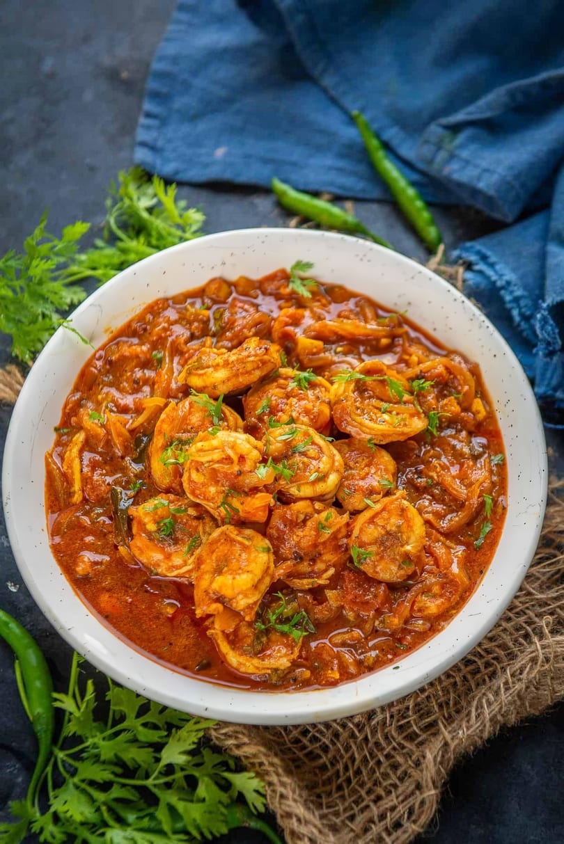 A white bowl filled with shrimp curry, garnished with fresh cilantro, on a dark surface.